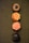 Four cupcakes are neatly arranged in a vertical line on a textured green surface. Each cupcake has distinct frosting designs and colors. The top cupcake has chocolate frosting with a central glossy decoration, resembling a flower or sun. The second cupcake features orange and yellow star-like icing patterns. The third cupcake displays a swirl of pink frosting adorned with small colorful sprinkles. The bottom cupcake has a richly dark chocolate frosting with a glossy finish.