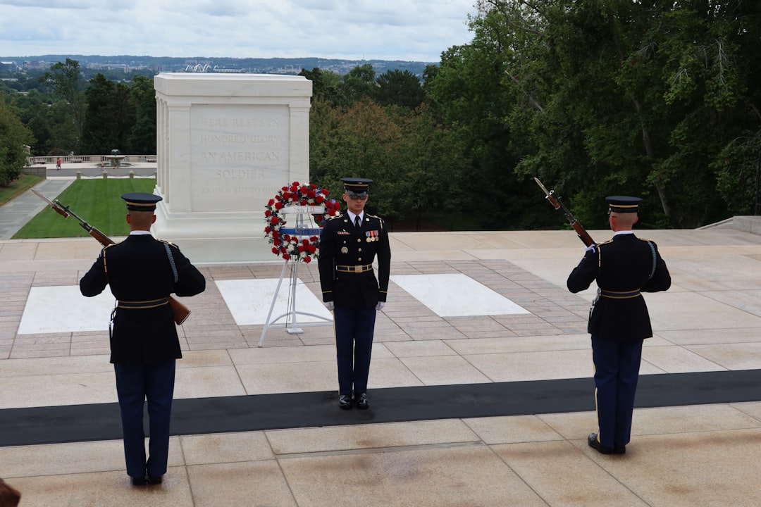 a group of men in military uniforms holding guns and a wreath with Tomb of the Unknowns in the background