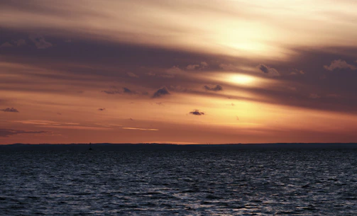 A serene tropical sunset over calm ocean waters with soft golden light.