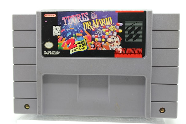 A gray Super Nintendo Entertainment System (SNES) cartridge displaying the label for 'Tetris & Dr. Mario'. The label features colorful graphics, including falling blocks from Tetris and Dr. Mario characters like Mario, viruses, and capsules. It also includes the Nintendo logo and information indicating it's a game for one or two players.