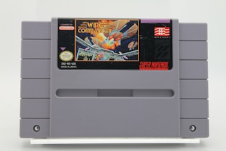 A Super Nintendo Entertainment System (SNES) game cartridge featuring the game 'Wing Commander.' The label displays a space-themed image with spaceships engaged in a battle, and the Nintendo and Mindscape logos are visible.