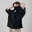 A person is pulling a black oversized shirt over their face, revealing only their eyes. The shirt features a white graphic logo and the word 'social'. The person has light brown hair and is standing against a neutral background, wearing light-colored pants.