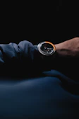 Close-up of a man adjusting a sleek watch against a dark background.