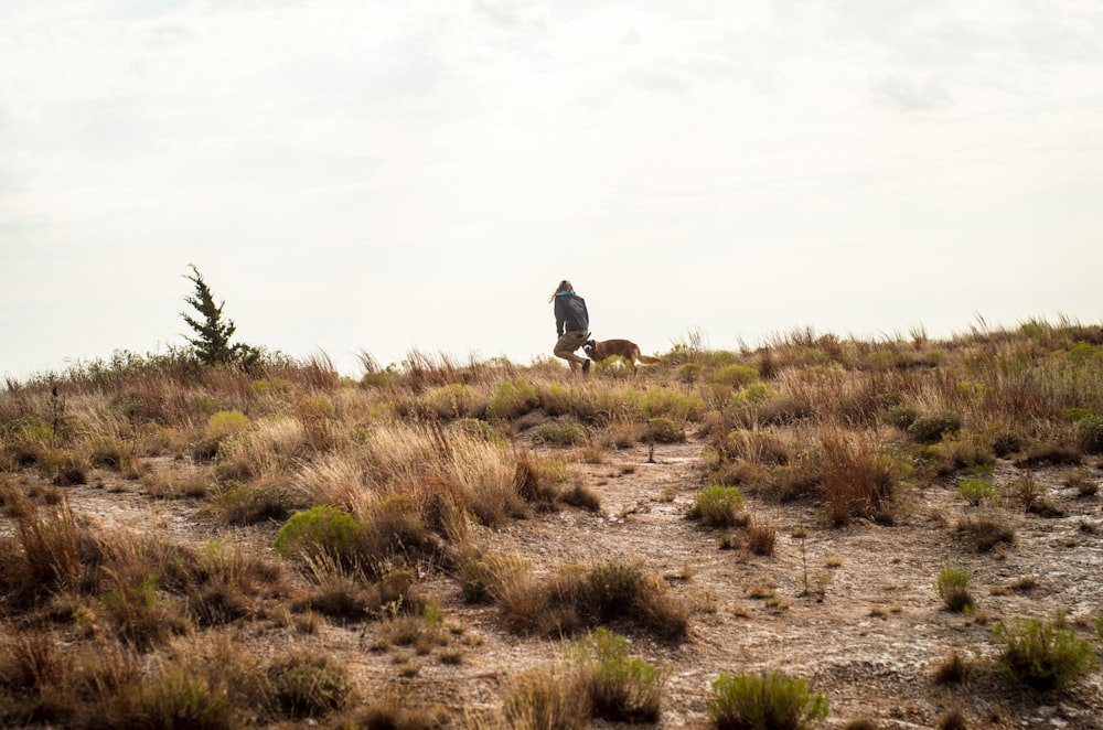 a person and a dog walking on a dirt path in a grassy area