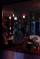 A dimly lit room features modern furniture, including curved chairs and a large, reflective Rotalux light reflector. The walls have vertical slits creating patterns with the light. Several spherical lights hang from the ceiling, adding to the atmospheric and stylish ambiance. There is a blend of deep reds, blues, and subtle oranges creating a cozy yet sophisticated interior space.