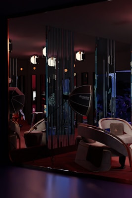 A dimly lit room features modern furniture, including curved chairs and a large, reflective Rotalux light reflector. The walls have vertical slits creating patterns with the light. Several spherical lights hang from the ceiling, adding to the atmospheric and stylish ambiance. There is a blend of deep reds, blues, and subtle oranges creating a cozy yet sophisticated interior space.