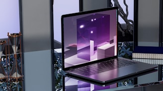 A sleek, modern laptop placed on a reflective glass surface. The screen displays abstract, geometric shapes in shades of purple with bright highlights. To the left, two hourglasses with gold frames are seen. In the background, blurred objects and a potted plant provide an industrial yet sophisticated ambiance.