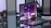 A sleek, modern laptop placed on a reflective glass surface. The screen displays abstract, geometric shapes in shades of purple with bright highlights. To the left, two hourglasses with gold frames are seen. In the background, blurred objects and a potted plant provide an industrial yet sophisticated ambiance.