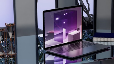 A sleek, modern laptop placed on a reflective glass surface. The screen displays abstract, geometric shapes in shades of purple with bright highlights. To the left, two hourglasses with gold frames are seen. In the background, blurred objects and a potted plant provide an industrial yet sophisticated ambiance.
