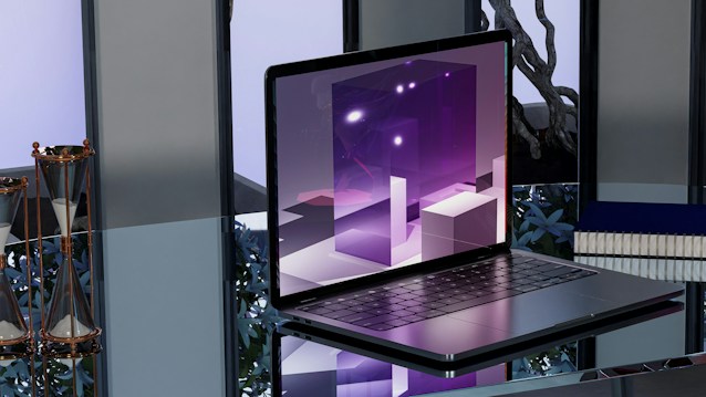 A sleek, modern laptop placed on a reflective glass surface. The screen displays abstract, geometric shapes in shades of purple with bright highlights. To the left, two hourglasses with gold frames are seen. In the background, blurred objects and a potted plant provide an industrial yet sophisticated ambiance.