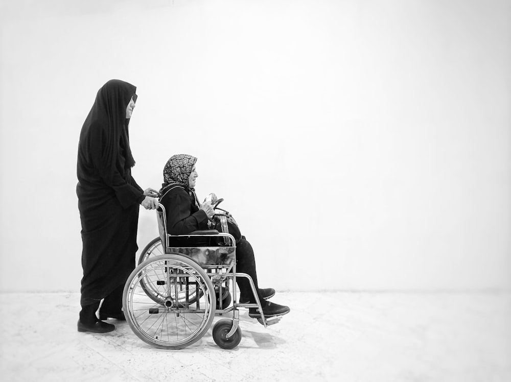 uma pessoa em um manto preto empurrando um bebê em uma cadeira de rodas