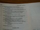 An open Bible displaying text from Psalm 150:6. The page is slightly curved and the text is in a serif font. Lighting is soft, creating a warm and inviting atmosphere.