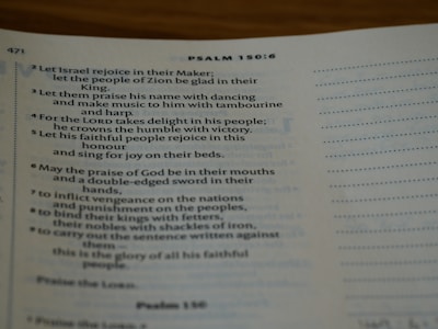 An open Bible displaying text from Psalm 150:6. The page is slightly curved and the text is in a serif font. Lighting is soft, creating a warm and inviting atmosphere.
