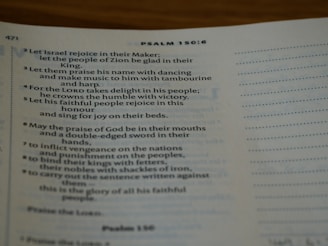An open Bible displaying text from Psalm 150:6. The page is slightly curved and the text is in a serif font. Lighting is soft, creating a warm and inviting atmosphere.