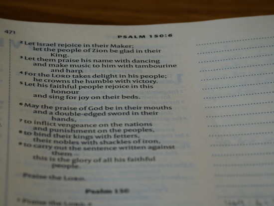 An open Bible displaying text from Psalm 150:6. The page is slightly curved and the text is in a serif font. Lighting is soft, creating a warm and inviting atmosphere.