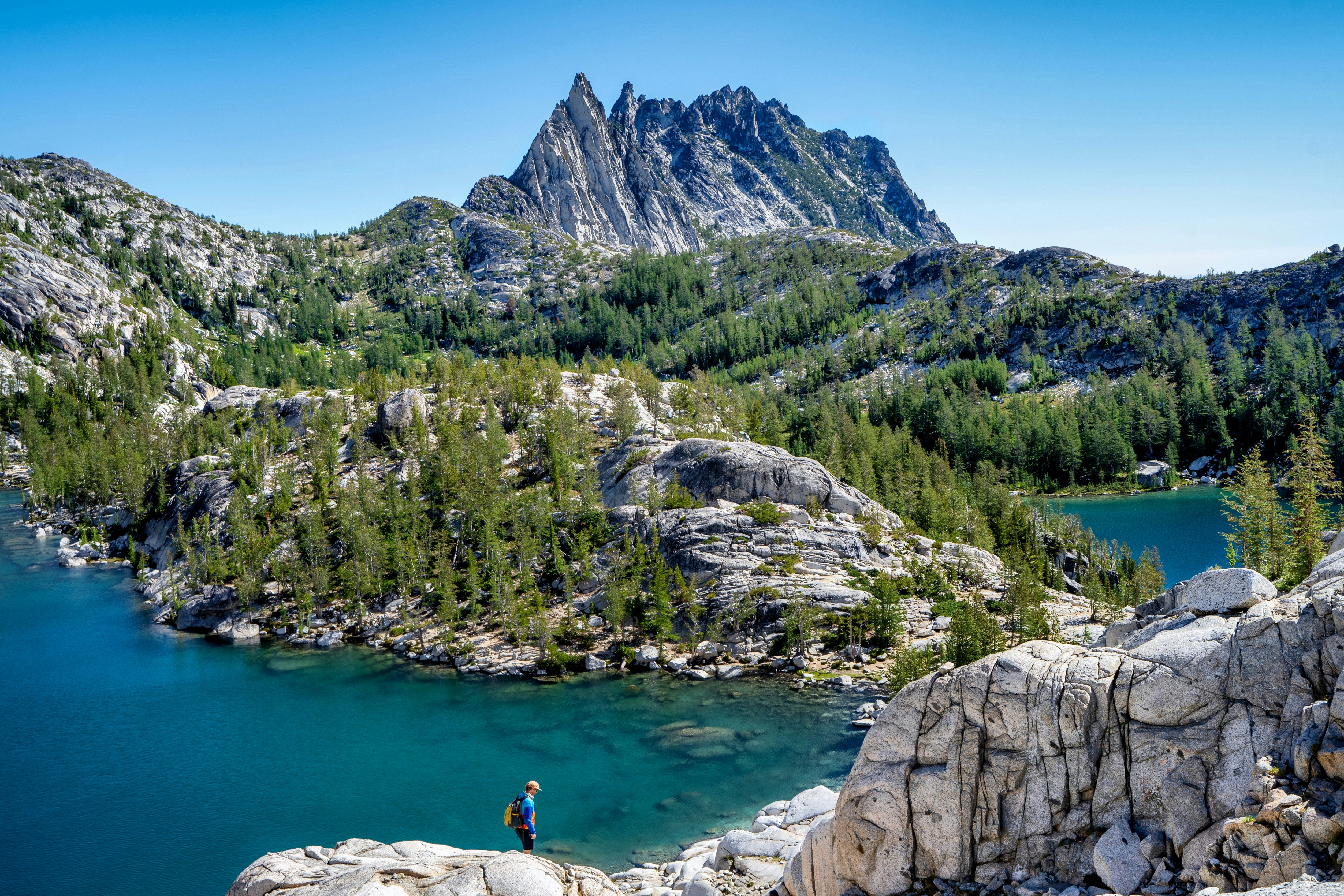 a person standing on a rocky shore by a lake and mountains