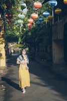 A sunlit street scene featuring a woman in a flowing pastel dress and oversized sunglasses.