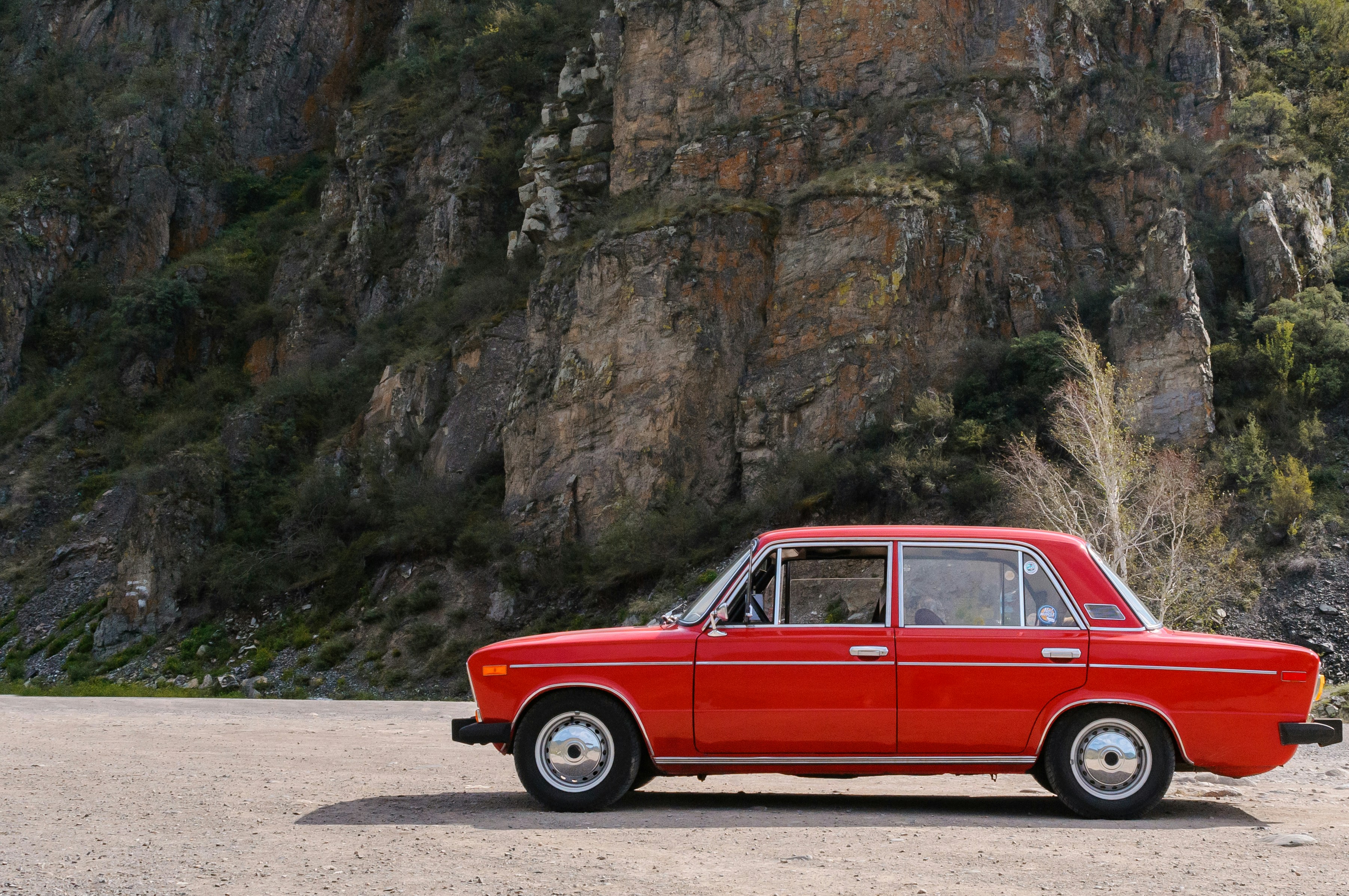a red car parked in front of a rocky cliff