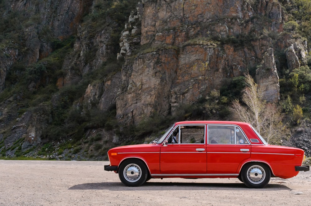 a red car parked in front of a rocky cliff