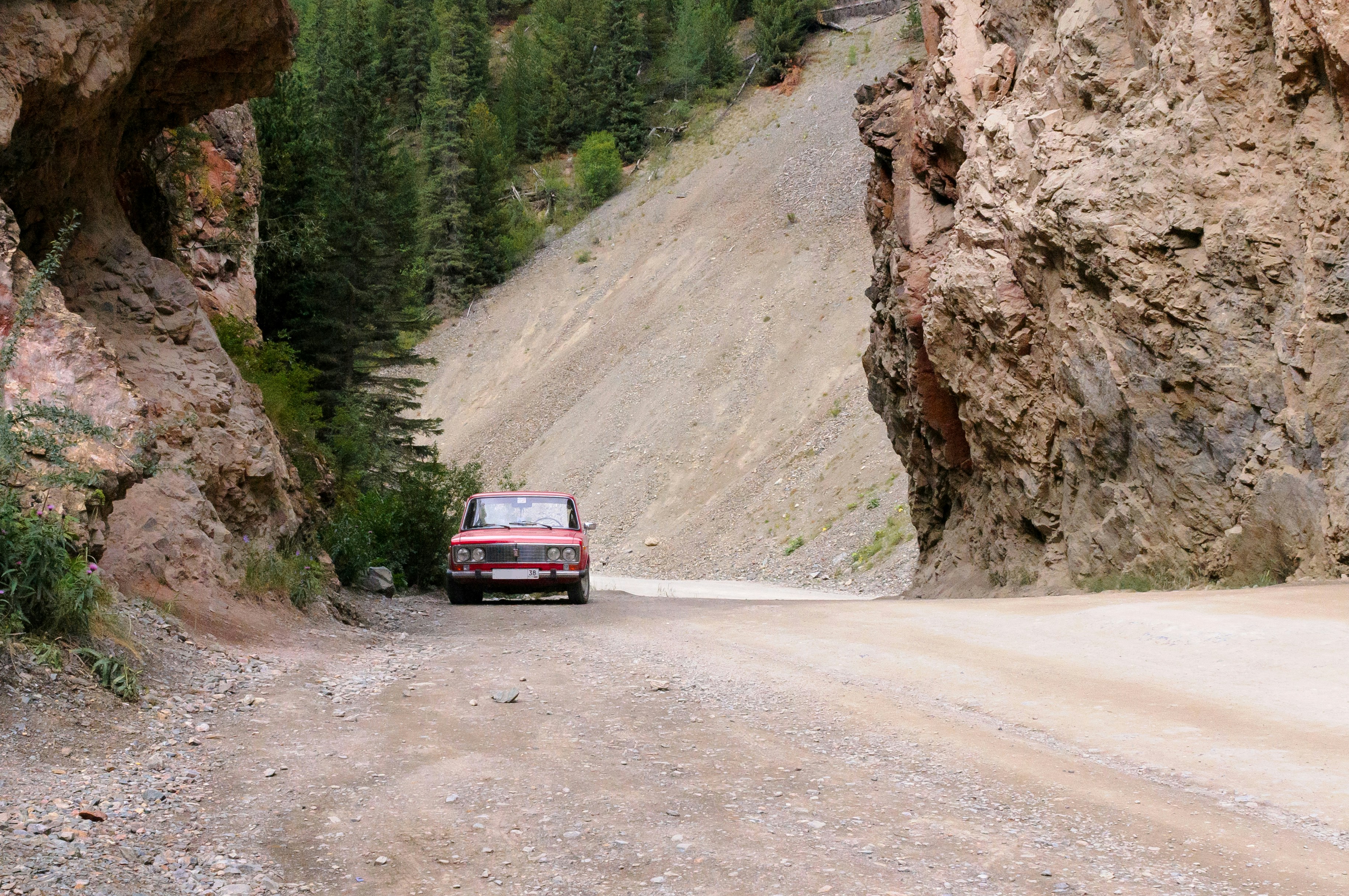 a red car driving on a dirt road between rocky cliffs