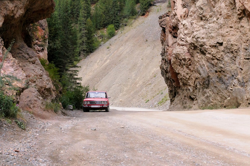 a red car driving on a dirt road between rocky cliffs