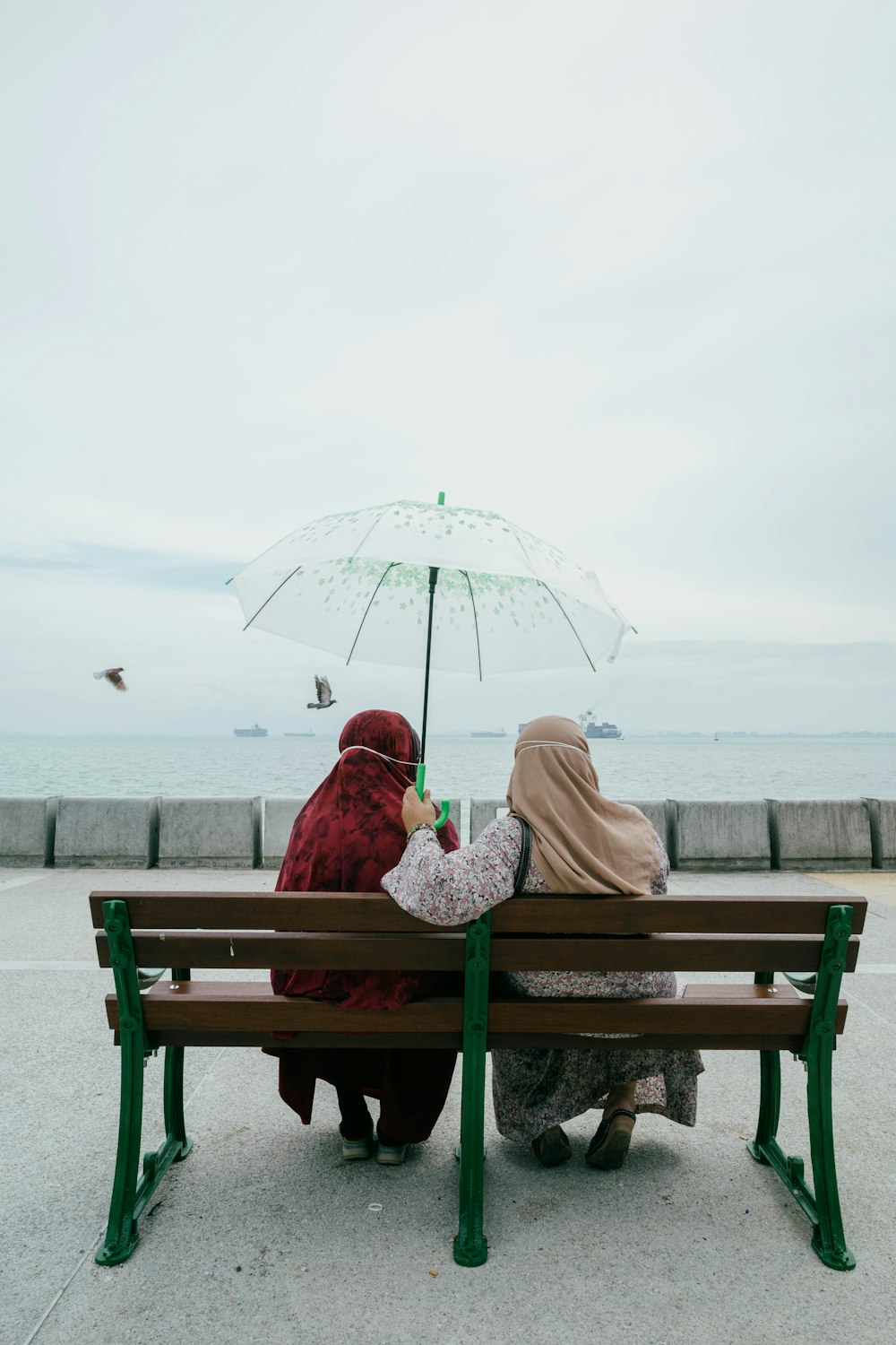 a couple of women sit on a bench under an umbrella