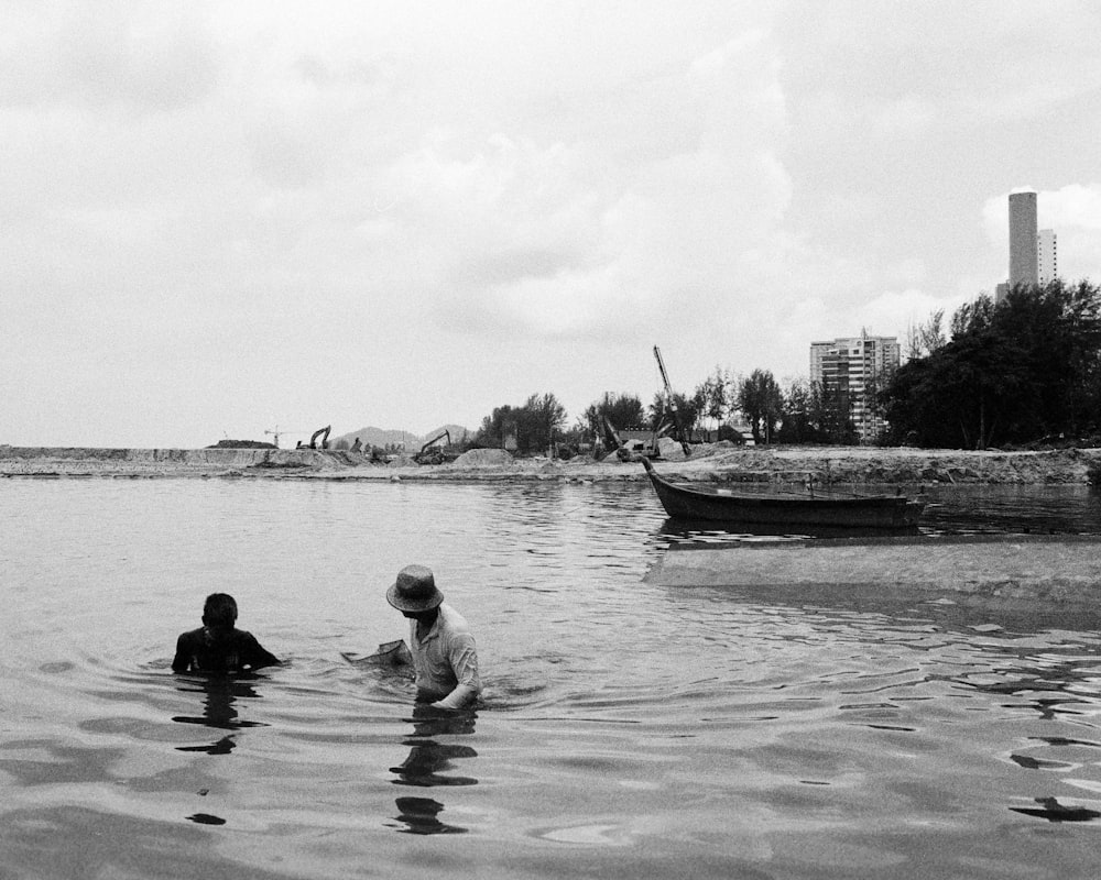 a couple of people in a body of water with a boat in the background