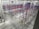 An industrial warehouse with multiple rows of blue and red metal storage racks. The floor is concrete, and the warehouse is well-lit with high ceiling lights. A fire extinguisher is located at the lower-left corner of the warehouse.