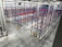 An industrial warehouse with multiple rows of blue and red metal storage racks. The floor is concrete, and the warehouse is well-lit with high ceiling lights. A fire extinguisher is located at the lower-left corner of the warehouse.