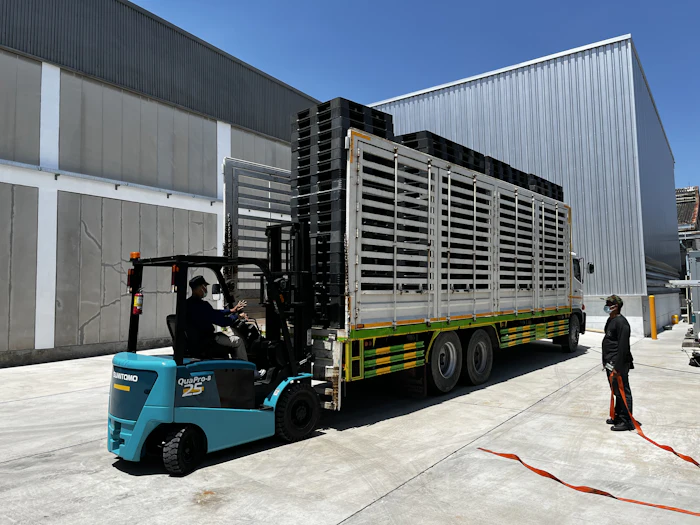 Forklift loading pallets onto a truck beside a warehouse