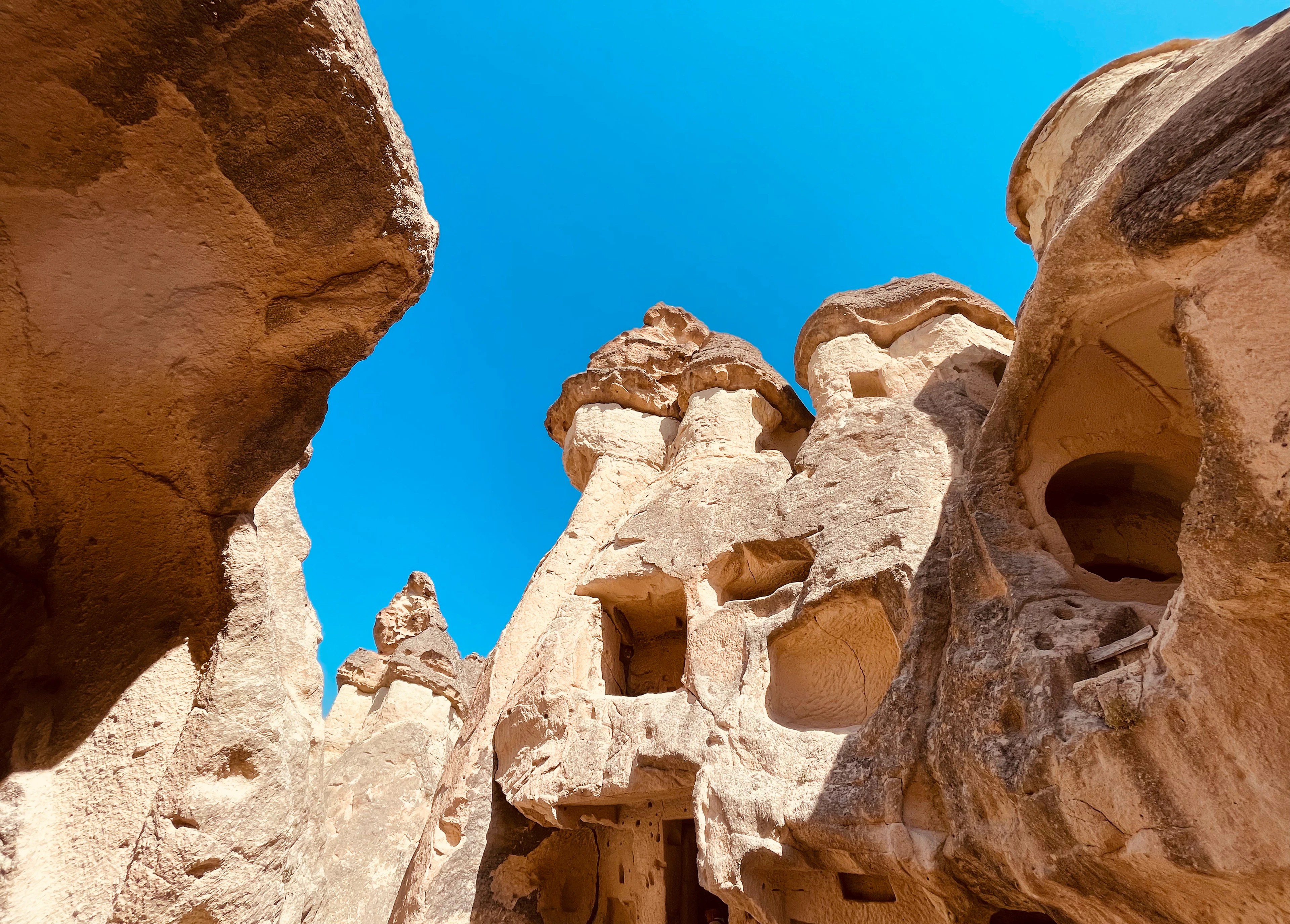 Looking straight up between clustered fairy chimney spires against a vivid blue sky.