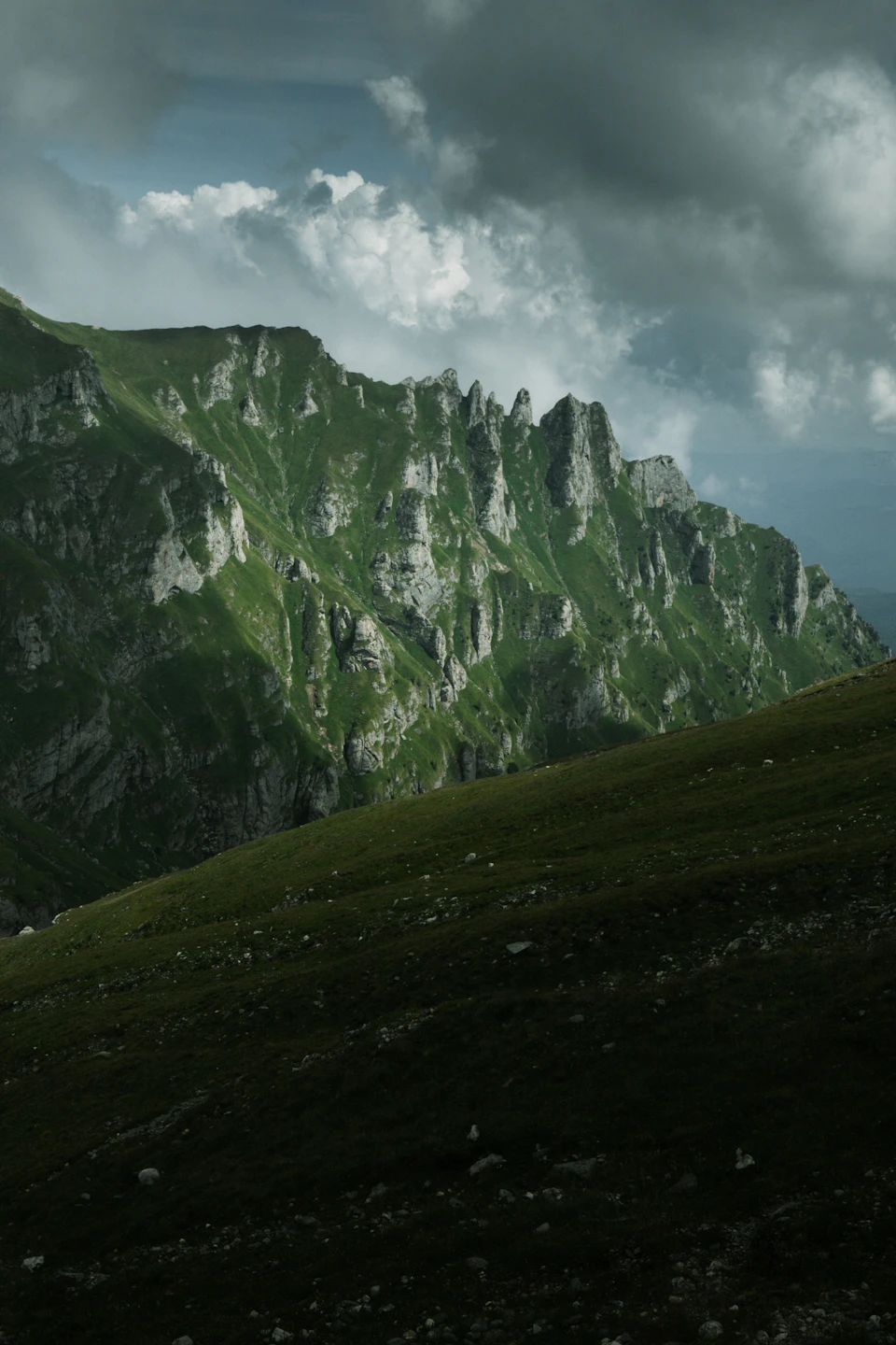 Majestic mountain range with green cliffs and grassy slope, set against a vibrant sky backdrop