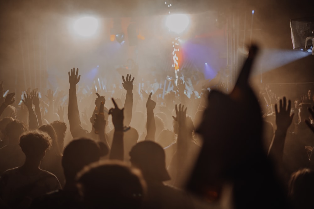 Una folla di persone con le mani alzate in aria davanti a un palco con le luci