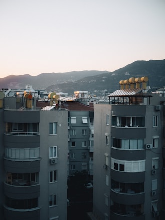 Mid-rise apartment buildings under a soft, early evening sky with distant mountains as a backdrop. The rooftops are equipped with solar water heaters, casting a warm glow from the setting sun.