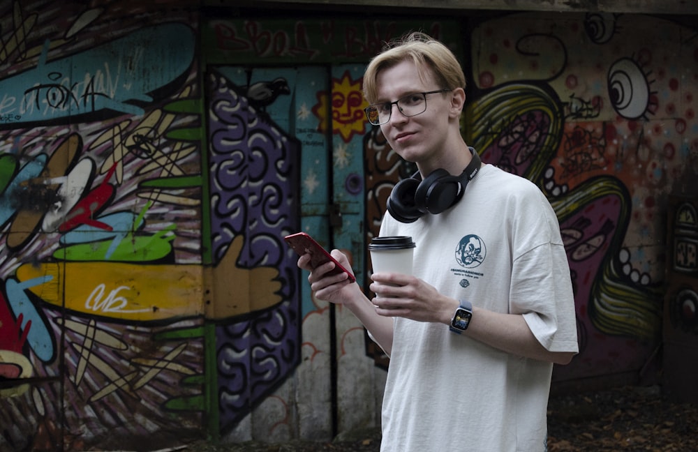 Un homme portant des écouteurs et tenant une tasse devant un mur avec des graffitis
