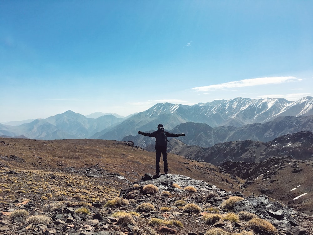 a person standing on a rocky hill with mountains in the background