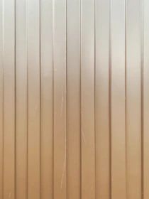 Vertical metal panels with evenly spaced groves running from top to bottom. The surface is slightly reflective with some visible scratches and lines.