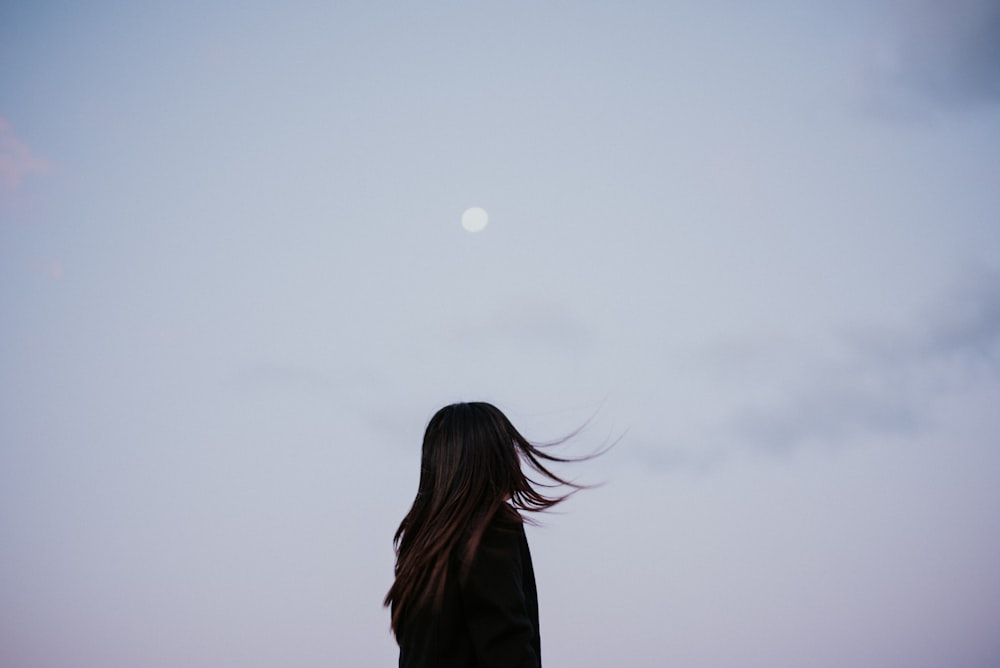 a woman standing in front of a full moon