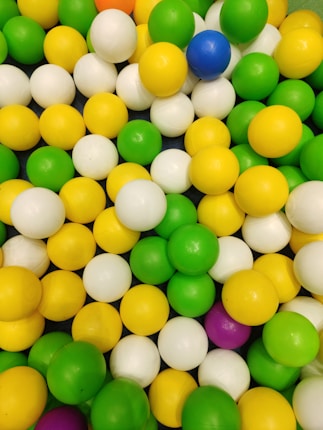 A collection of colorful plastic balls in various shades including green, yellow, white, and occasional blue and purple. The balls appear to be arranged randomly in a pile.