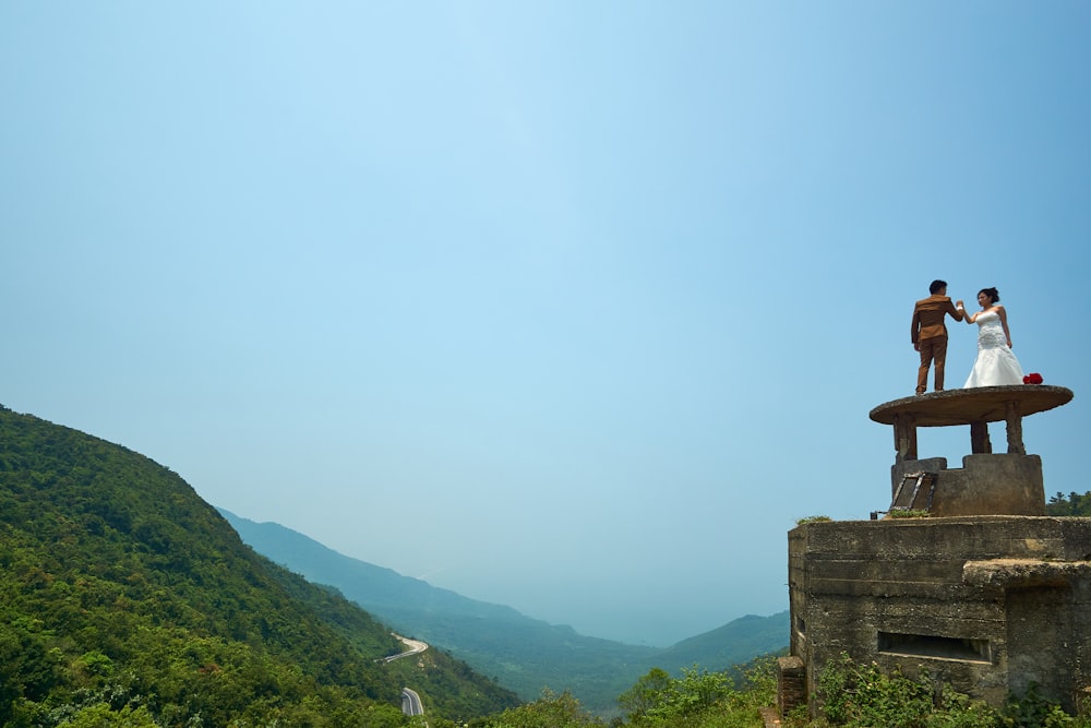 a couple of people on a stone structure with mountains in the background