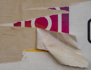Peeling layers of paper reveal parts of an underlying image, including a portion with red and purple colors and fragments of what appear to be letters or shapes.
