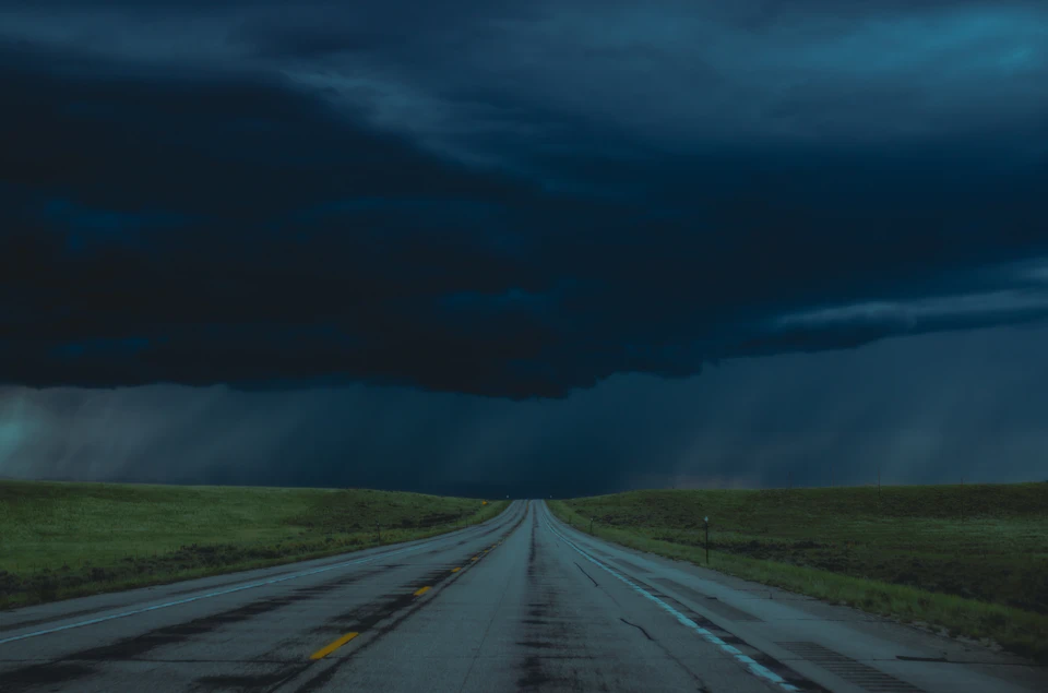 Long, straight highway stretches into distance under dark cloudy sky with empty road ahead