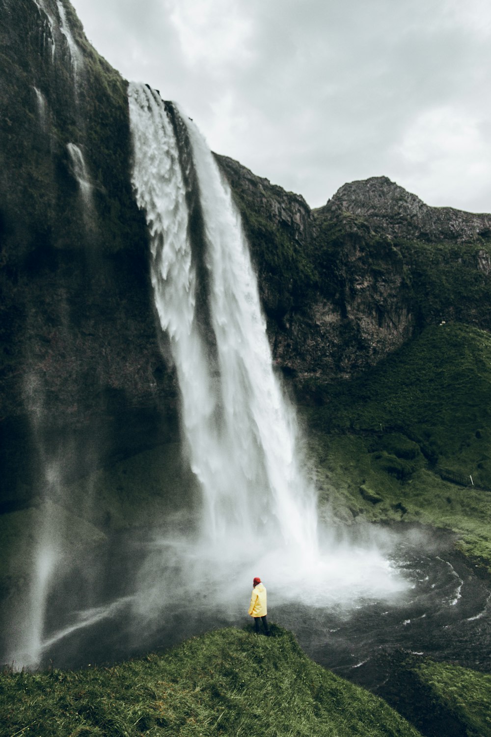 a person standing on a cliff with a waterfall and a large waterfall