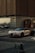 A luxury sports car with a sleek design and distinctive headlights is parked on a street. It is positioned near a modern building with horizontal paneling and next to a shop with a sign that reads 'TATTOO'. A small golf cart is also visible in the background, and a sign indicating VIP parking is placed in front of the car.