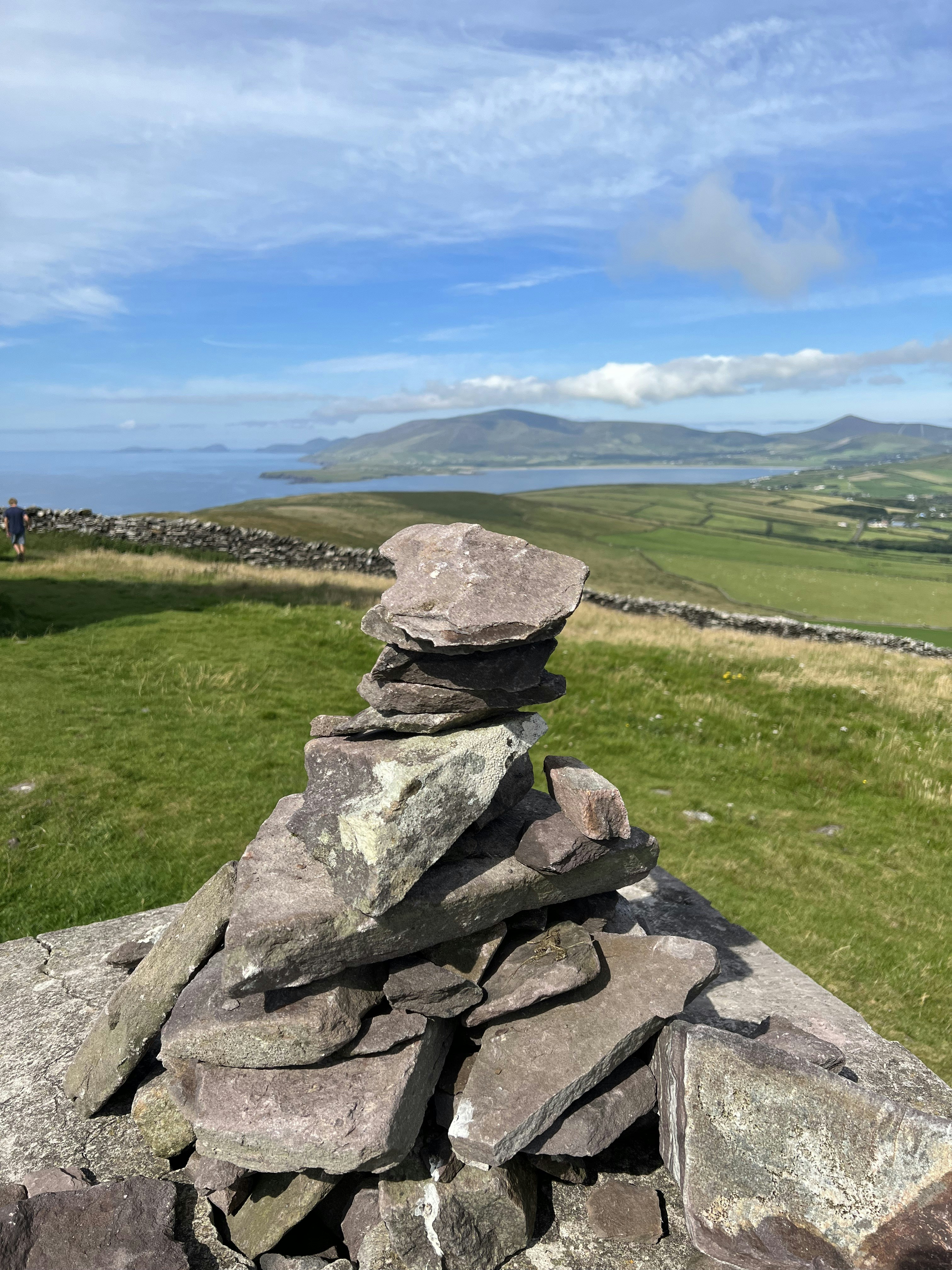a stack of rocks on a grassy hill overlooking a body of water