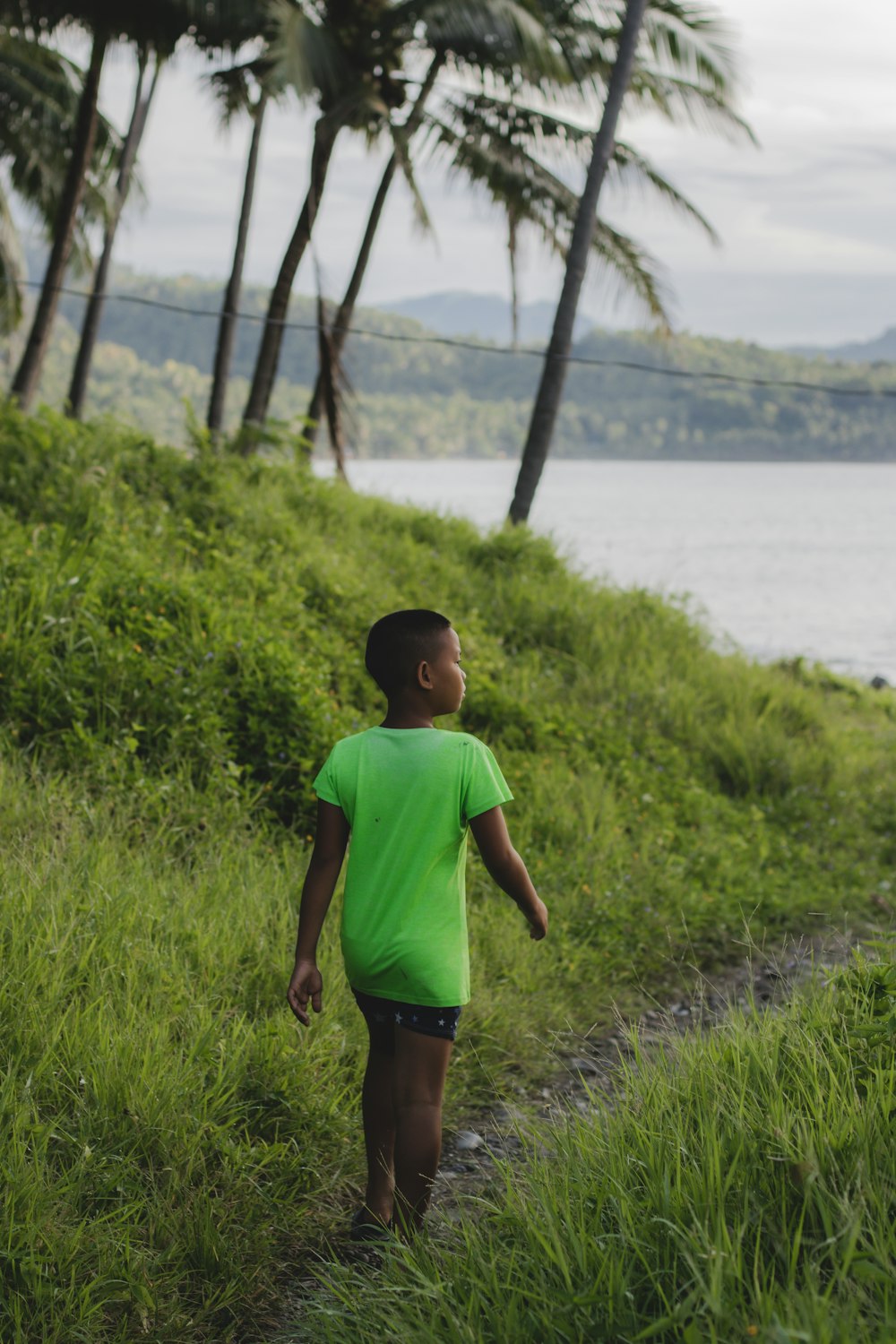 a boy standing in a grassy area next to a body of water