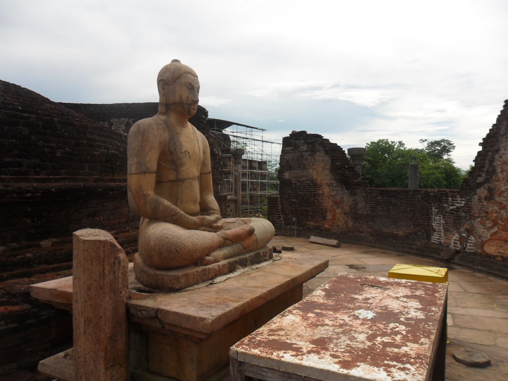 a statue of a man sitting on a bench in front of a stone wall