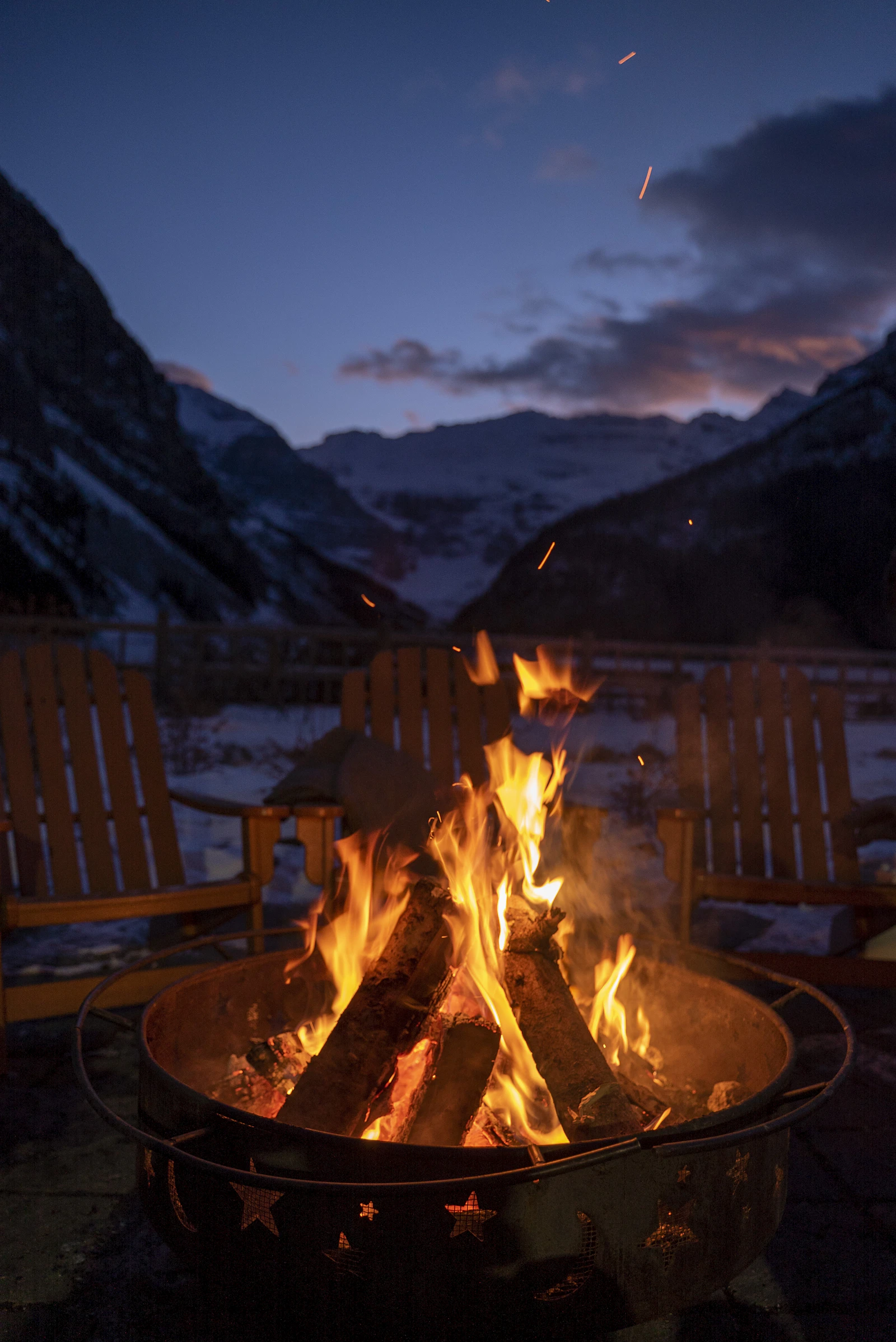 Fire pit on a deck beside a lake with mountains in the background