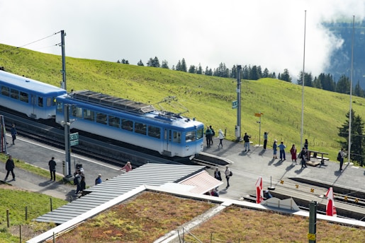 A traveler consulting a map beside a scenic Swiss train station surrounded by alpine scenery.