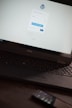 A laptop displaying a WordPress login screen with fields for username and password. The screen has options to log in with Telegram or email. The logo of WordPress is visible on top. A smartphone is resting on the surface near the laptop.